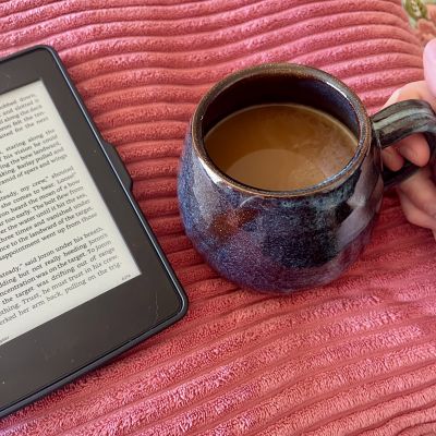 Image of an open kindle next to handmade blue mug filled with coffee.